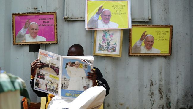 Мужчина читает газету Catholic Mirror на фоне портретов Папы Римского в Найроби, Кения Мужчина читает газету Catholic Mirror на фоне портретов Папы Римского в Найроби, Кения
