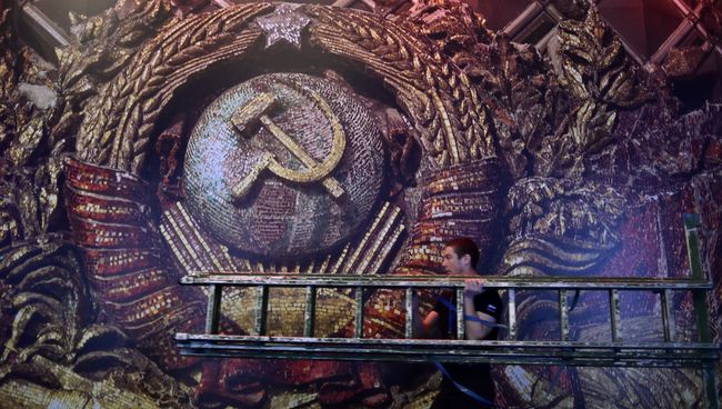 Рабочий с лестницей на фоне изображения герба СССР. Архивное фото Рабочий с лестницей на фоне изображения герба СССР. Архивное фото