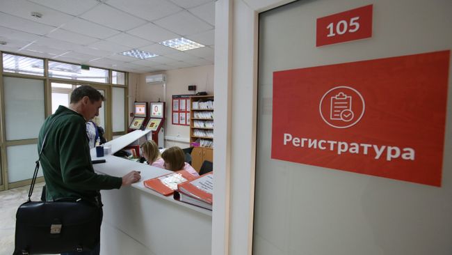 Посетитель у регистрационного стола в поликлинике. Архивное фото Посетитель у регистрационного стола в поликлинике. Архивное фото