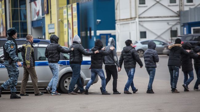 Сотрудник полиции ведет задержанных во время рейда на территории торгового-ярмарочного комплекса Москва в Люблино Сотрудник полиции ведет задержанных во время рейда на территории торгового-ярмарочного комплекса Москва в Люблино
