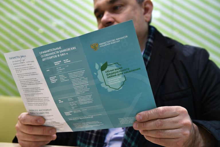 Мужчина в одном из отделений Сбербанка изучает буклет о приобретении облигаций федерального займа
