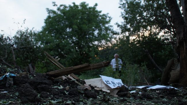 Местный житель стоит у воронки от снаряда во дворе соседского дома в Донбассе. Архивное фото Местный житель стоит у воронки от снаряда во дворе соседского дома в Донбассе. Архивное фото