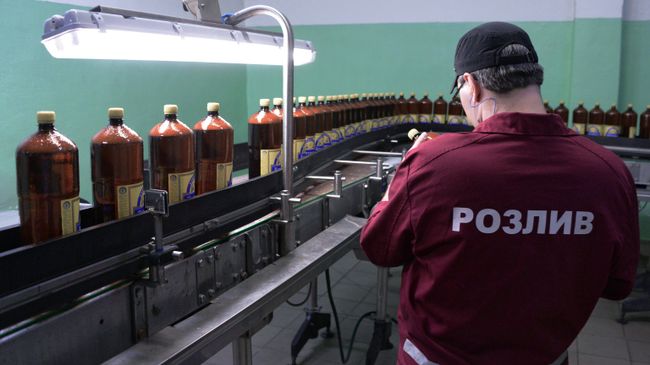 Сотрудник у линии розлива пива в полиэтиленовые бутылки в цехе розлива пива. Архивное фото Сотрудник у линии розлива пива в полиэтиленовые бутылки в цехе розлива пива. Архивное фото