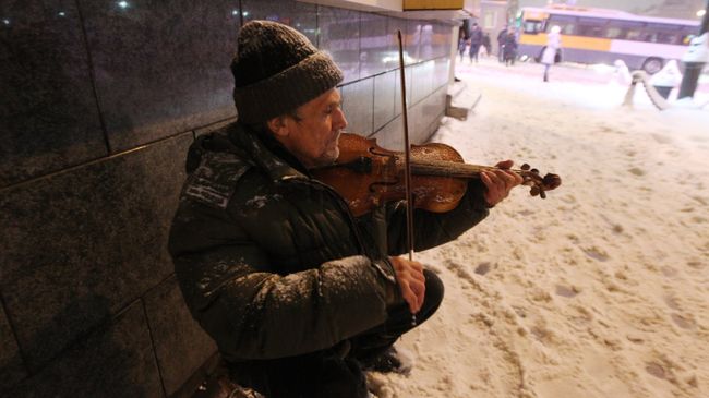 Мужчина играет на скрипке на улице во время снегопада
