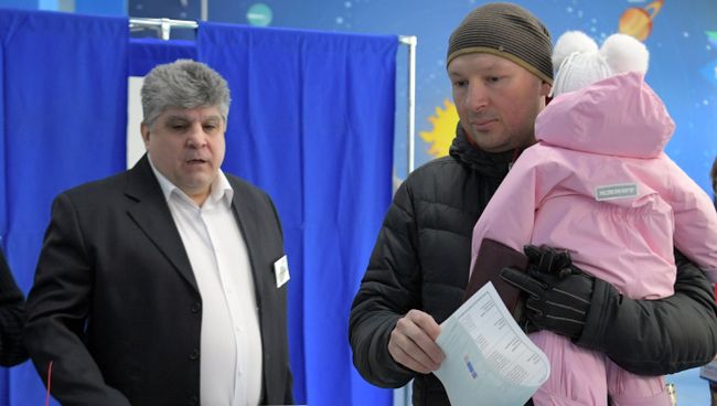 Мужчина с ребенком во время голосования на выборах президента РФ на избирательном участке № 90 в Москве. 18 марта 2018 Мужчина с ребенком во время голосования на выборах президента РФ на избирательном участке № 90 в Москве. 18 марта 2018