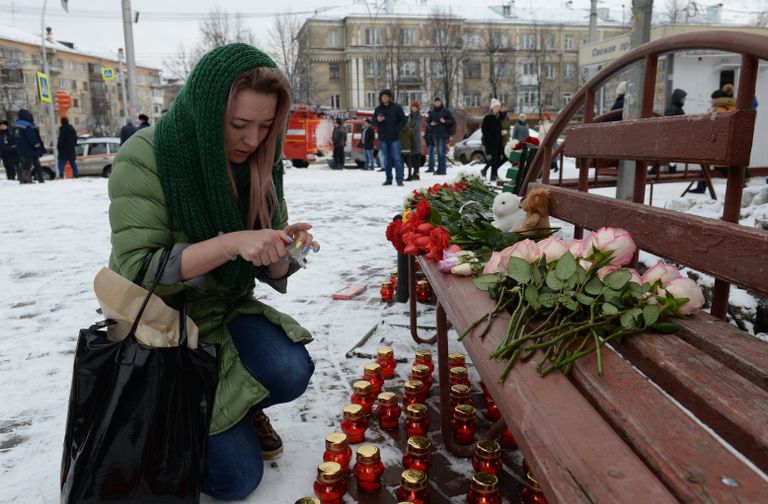 Женщина зажигает свечу возле здания торгового центра «Зимняя вишня» в Кемерово, где произошел пожар Женщина зажигает свечу возле здания торгового центра «Зимняя вишня» в Кемерово, где произошел пожар