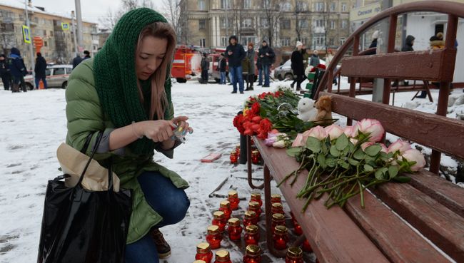 Женщина зажигает свечу возле здания торгового центра «Зимняя вишня» в Кемерово, где произошел пожар Женщина зажигает свечу возле здания торгового центра «Зимняя вишня» в Кемерово, где произошел пожар