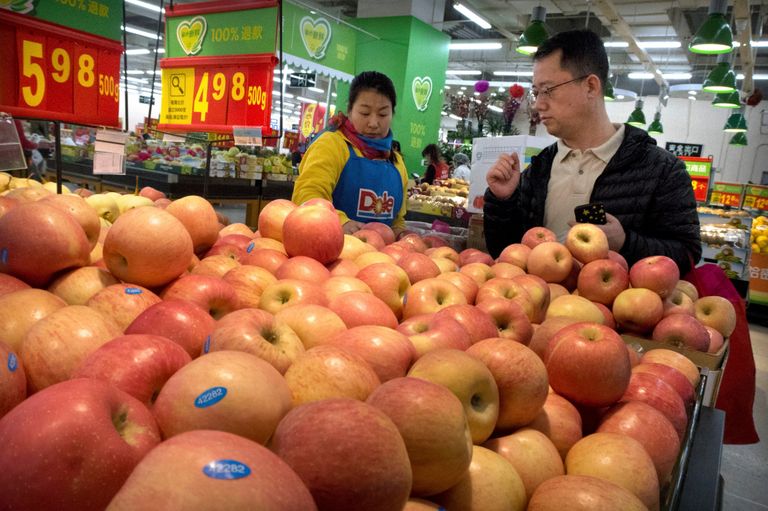 Женщина в униформе с логотипом американской продуктовой компании помогает покупателю выбрать яблоки в супермаркете в Пекине Женщина в униформе с логотипом американской продуктовой компании помогает покупателю выбрать яблоки в супермаркете в Пекине