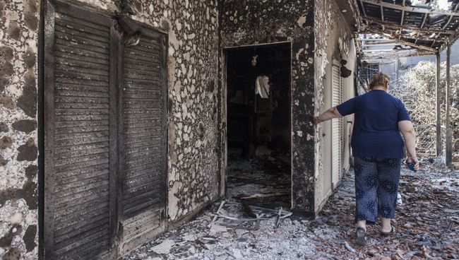 Женщина у своего дома, пострадавшего в результате лесных пожаров, в поселении Мати в Греции. 25 июля 2018