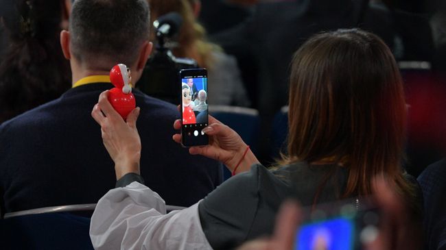 Журналистка фотографирует неваляшку во время ежегодной большой пресс-конференции президента РФ Владимира Путина Журналистка фотографирует неваляшку во время ежегодной большой пресс-конференции президента РФ Владимира Путина