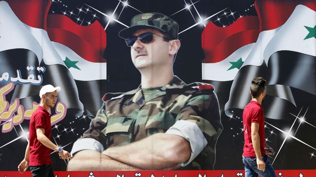 Сирийцы проходят мимо плаката с изображением Башара Асада в Дамаске Сирийцы проходят мимо плаката с изображением Башара Асада в Дамаске