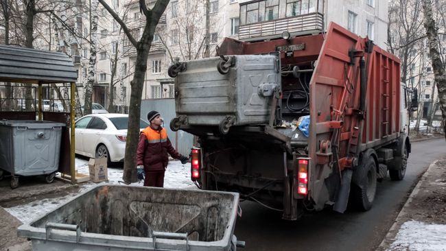 Сотрудник коммунальных служб выгружает мусор из контейнера в мусоровоз Сотрудник коммунальных служб выгружает мусор из контейнера в мусоровоз