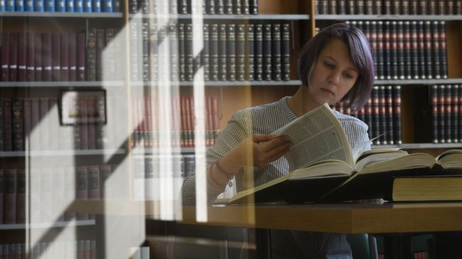 Девушка читает книгу в библиотеке Девушка читает книгу в библиотеке