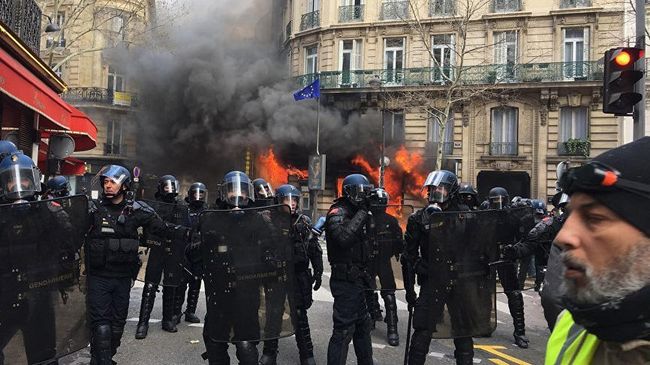 Полиция перед горящим зданием в Париже во время акции протеста желтых жилетов. 16 марта 2019 Полиция перед горящим зданием в Париже во время акции протеста желтых жилетов. 16 марта 2019
