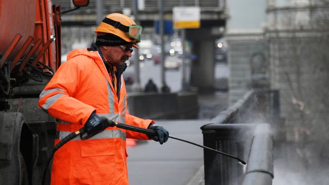 Сотрудник коммунальной службы моет ограду моста в Москве