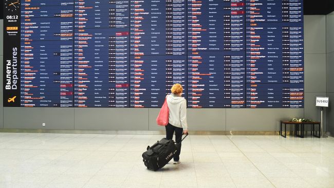 Женщина возле информационного табло с расписанием рейсов в аэропорту Шереметьево Женщина возле информационного табло с расписанием рейсов в аэропорту Шереметьево
