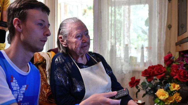 Волонтер помогает в настройке цифровой приставки дома у ветерана Великой Отечественной войны Афросиньи Белозеровой в городе Сочи Волонтер помогает в настройке цифровой приставки дома у ветерана Великой Отечественной войны Афросиньи Белозеровой в городе Сочи