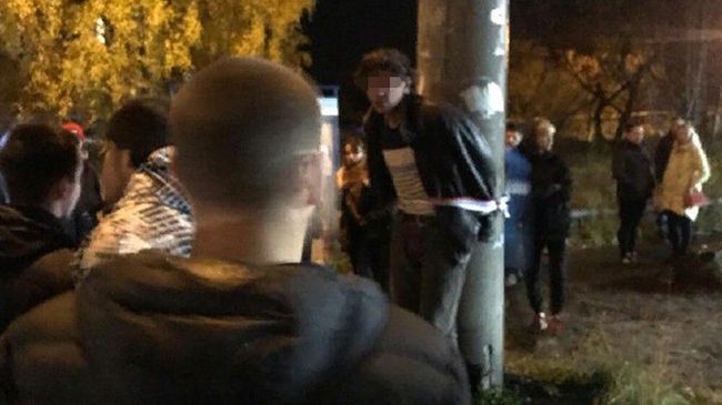 Мужчина, привязанный к столбу, в окружении десятков местных жителей. Цигломень