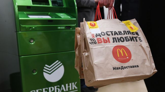 Посетитель совместного отделения Сбербанка и McDonalds в Москве стоит у банкомата с пакетами Макдоставки Посетитель совместного отделения Сбербанка и McDonalds в Москве стоит у банкомата с пакетами Макдоставки