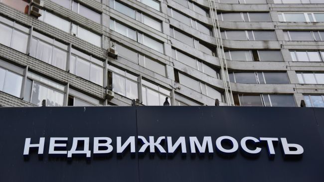 Вывеска с надписью Недвижимость на многоэтажном доме