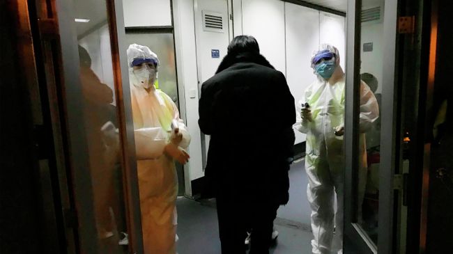 Медицинские работники в спецкостюмах проверяют температуру тела пассажиров, прибывающих из города Ухань в аэропорту Пекина Медицинские работники в спецкостюмах проверяют температуру тела пассажиров, прибывающих из города Ухань в аэропорту Пекина