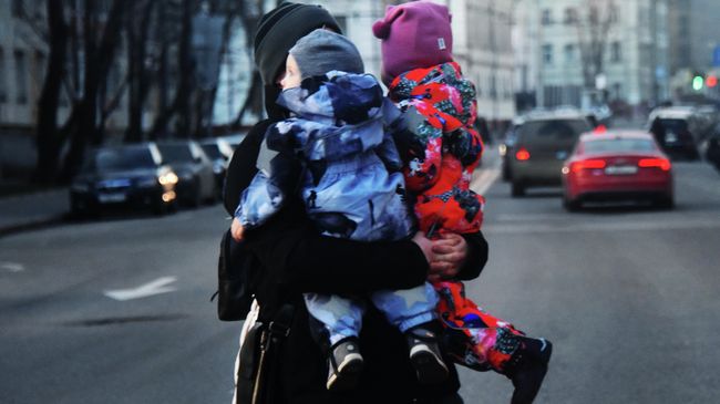 Женщина с двумя детьми на руках переходит дорогу Женщина с двумя детьми на руках переходит дорогу