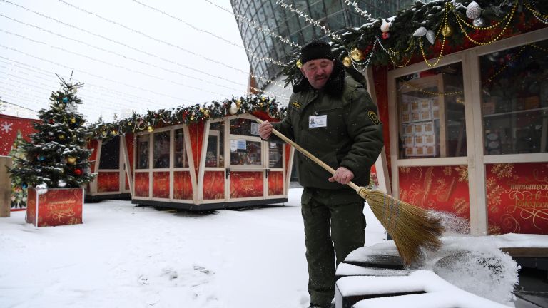 Мужчина убирает снег на площадке фестиваля Путешествие в Рождество в Москве