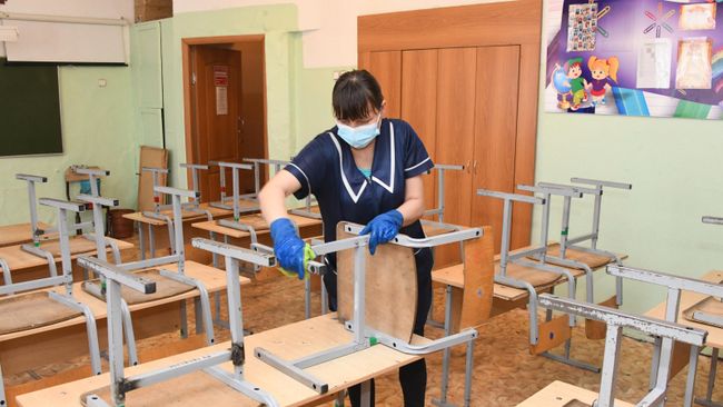 Сотрудница школы проводит санитарную обработку класса в школе Сотрудница школы проводит санитарную обработку класса в школе