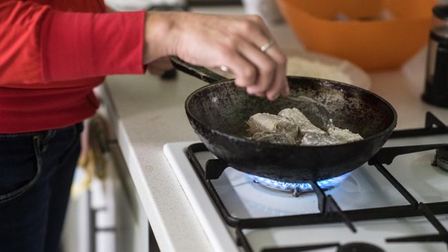 Женщина жарит рыбу на сковородке Женщина жарит рыбу на сковородке