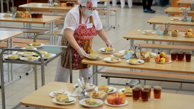 Работница школьной столовой разносит тарелки с едой к обеду учеников Работница школьной столовой разносит тарелки с едой к обеду учеников
