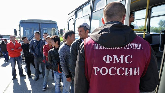 Сотрудник ФМС России с задержанными во время рейда на одном из рынков мигрантами, архивное фото
