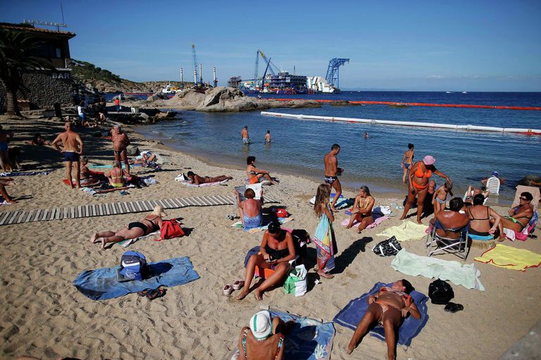 Люди отдыхают на пляже рядом с круизным лайнером Costa Concordia, где идет операция по его подъему Люди отдыхают на пляже рядом с круизным лайнером Costa Concordia, где идет операция по его подъему