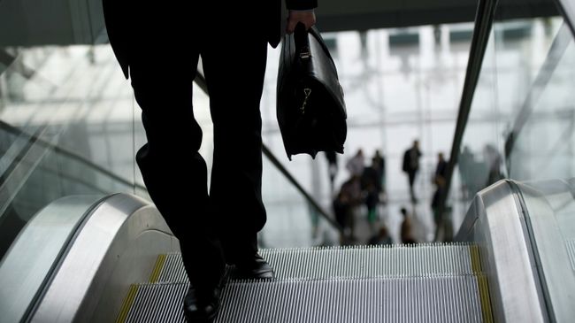 Мужчина с портфелем поднимается по эскалатору