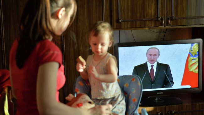 Молодая мама кормит ребенка во время просмотра трансляции обращения президента Владимира Путина. Архивное фото
