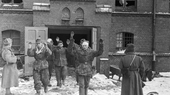 Пленные гитлеровцы выходят из дверей здания под конвоем советских бойцов.